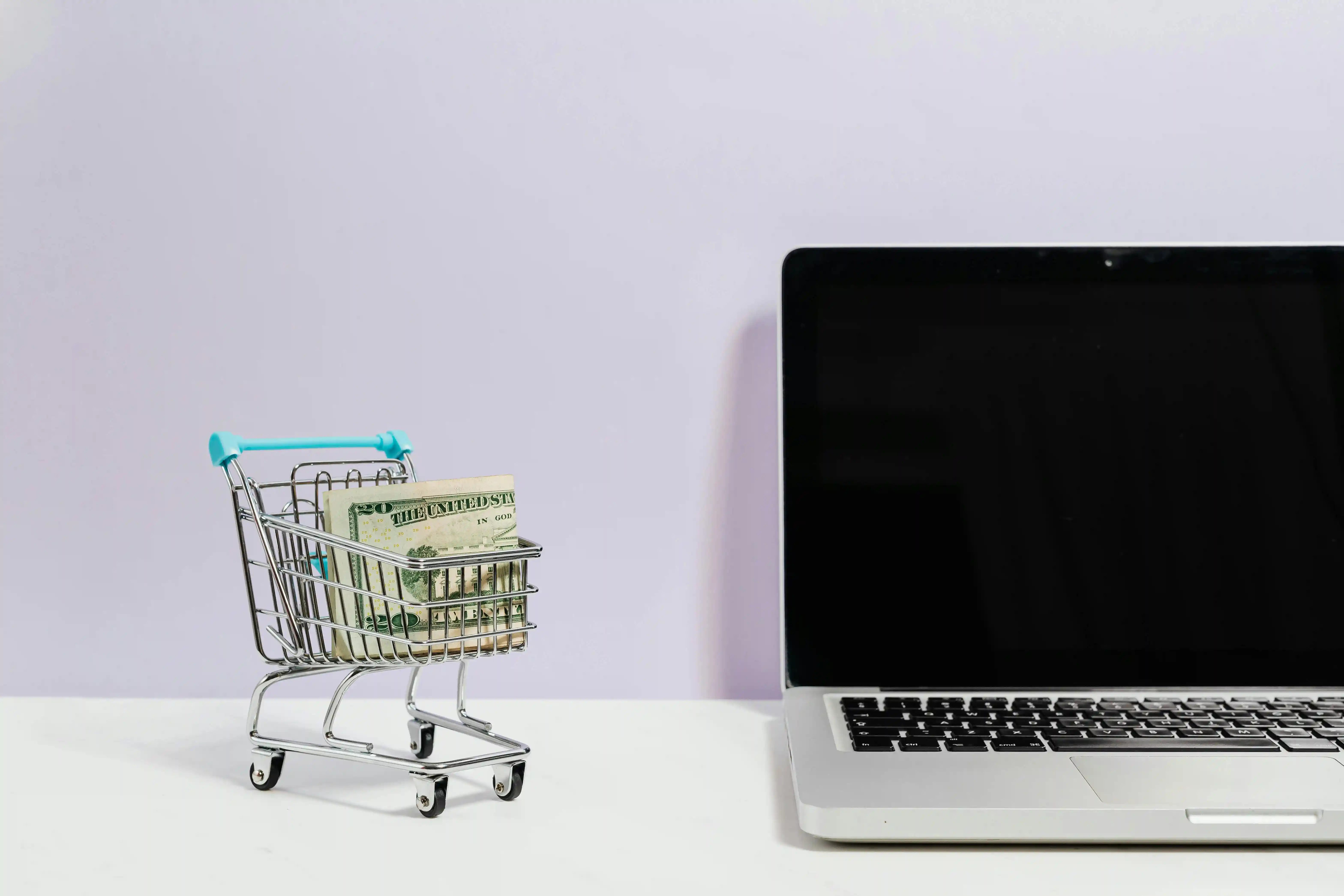 Foto van laptop met daarnaast een miniatuur winkelwagentje met daarin een rol Amerikaanse dollar
